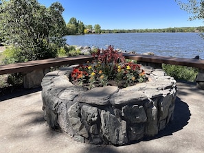 Enjoy a serene lakeside setting with a fire pit, walkway, and tranquil views of the lake surrounded by lush greenery.
