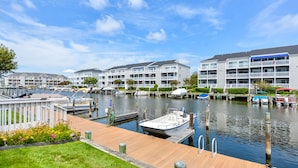 A marina with docked boats, a wooden pier, and a row of multi-story buildings with balconies. - Beautiful 2 BR 2 BA Unit on a Peaceful Canal with a Pool & Views of Fireworks (Ocean City)