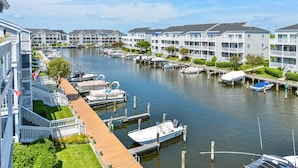 A marina with boats docked, a wooden walkway, and multi-story buildings with balconies. - Beautiful 2 BR 2 BA Unit on a Peaceful Canal with a Pool & Views of Fireworks (Ocean City)