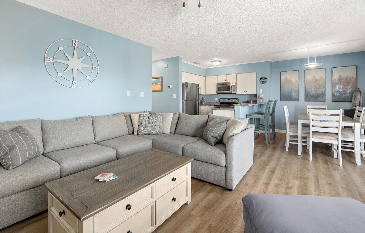 A modern living room with a sectional sofa, a wooden coffee table, and a dining area with white chairs.
