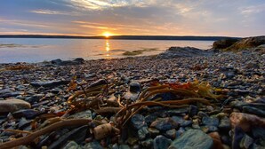 En klippefyldt kystlinje med en solnedgang over et roligt vand.