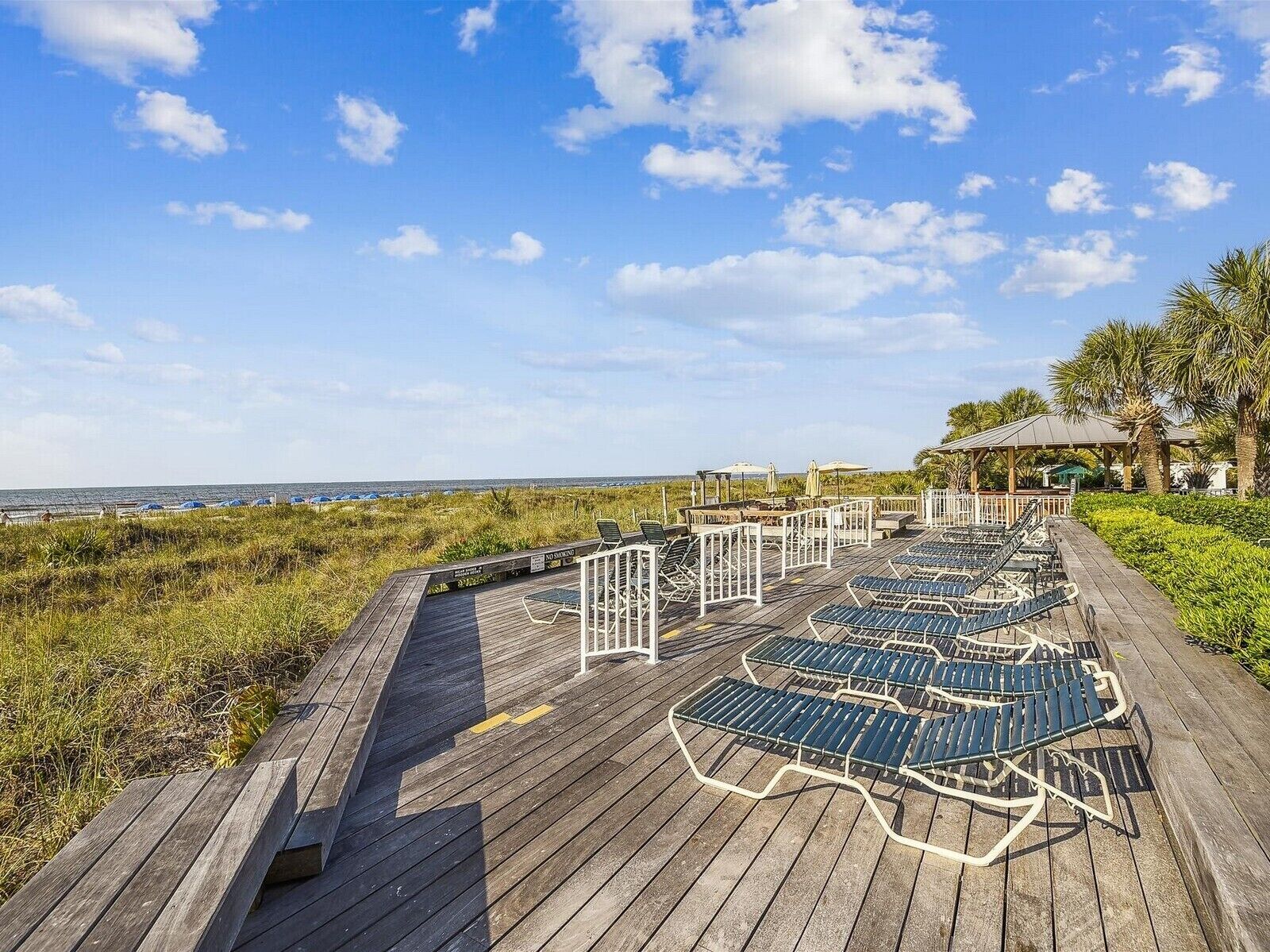 Een houten terras met ligbedden en een tuinhuisje met uitzicht op een strand.