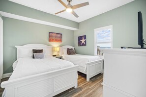 A bedroom with two beds, a ceiling fan, a window with blinds, and a wall with a star decoration.