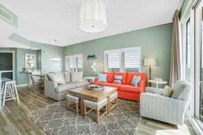 A living room with a grey sofa, an orange sofa, a small table, and a window with blinds.
