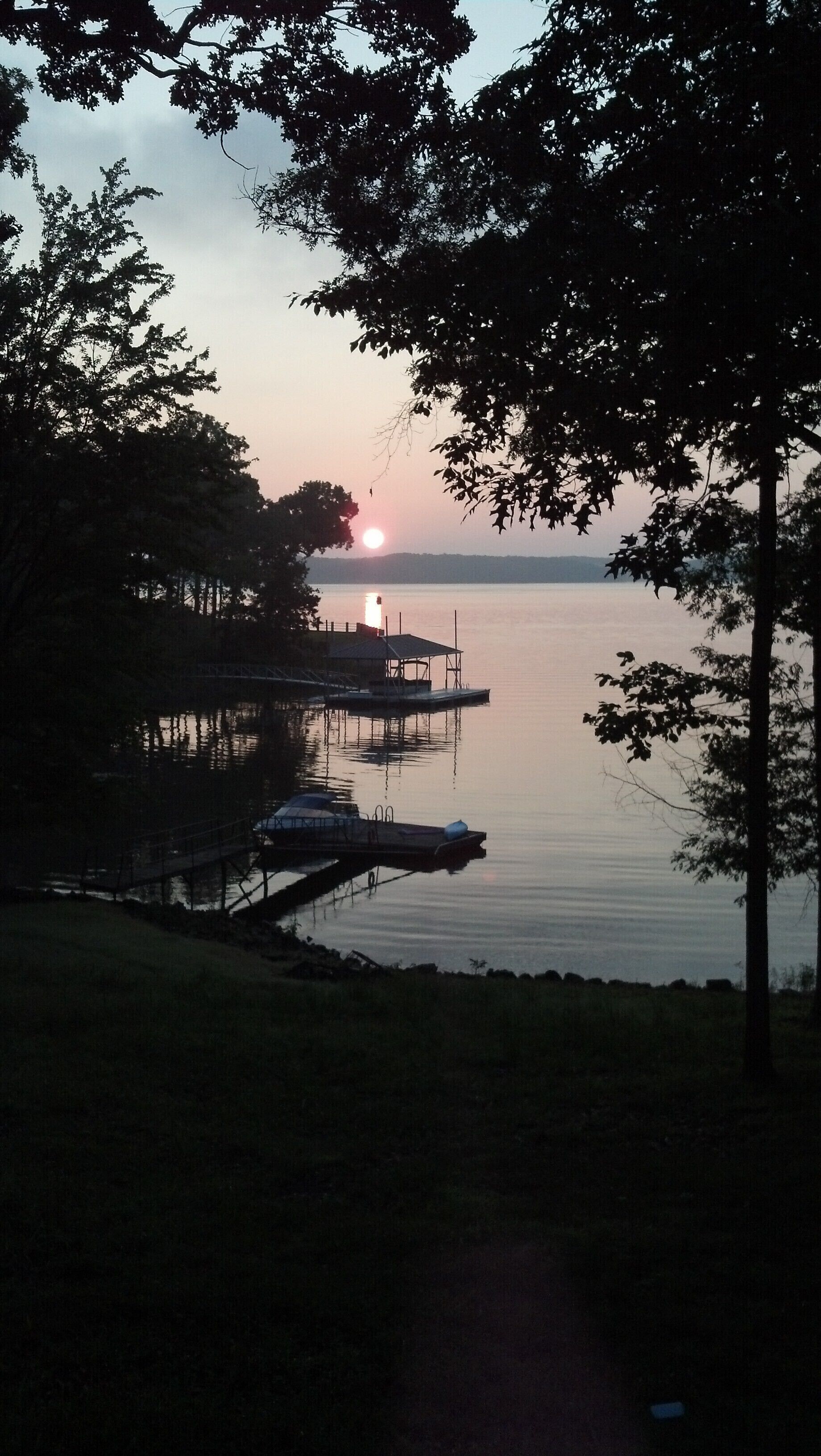 A lakeside view with a dock and boats, surrounded by trees.