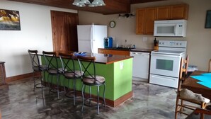 Une cuisine dotée d’un îlot central vert, de meubles en bois, d’un réfrigérateur blanc, d’un four à micro-ondes, d’un four traditionnel et d’un coin repas avec une table et des chaises.
