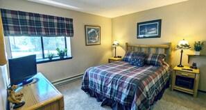 A bedroom with a bed, two bedside tables, a nightstand, a window with blinds, and a wall-mounted picture. - Spacious Condo w/ FREE WiFi, Parking, Heated Pool, Hot Tubs, Skier Shuttles (Avon)