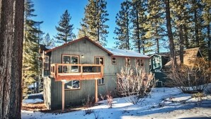 Une cabane à deux étages avec un balcon, entourée de neige et d’arbres.