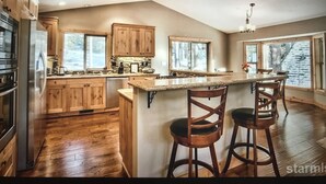 Une cuisine spacieuse avec des meubles en bois, un grand îlot central doté de tabourets de bar et une vue sur un paysage enneigé par les fenêtres.