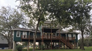 A two-story house with a wooden deck and stairs, surrounded by trees. - Green House on the River, Walk to Gruene Hall! (NEW BRAUNFELS)
