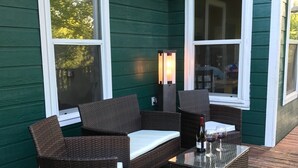 An outdoor patio with wicker furniture, a glass-top table, and a small lamp. - Green House on the River, Walk to Gruene Hall! (NEW BRAUNFELS)