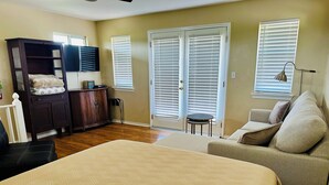 A bedroom with a large bed, a dresser, a chair, and a small table. There are two doors with white blinds and a window with blinds. - Green House on the River, Walk to Gruene Hall! (NEW BRAUNFELS)
