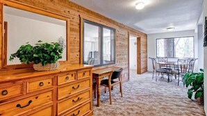 A room with a wooden dresser, a desk, and a dining table with chairs. There is a large window providing natural light.
