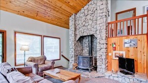 A cozy living room with a stone fireplace, wooden ceiling, and a TV on a wooden stand.