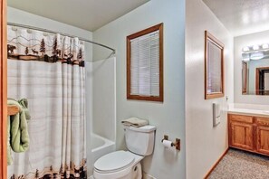 A bathroom with a toilet, a shower curtain with a forest design, and wooden cabinets.