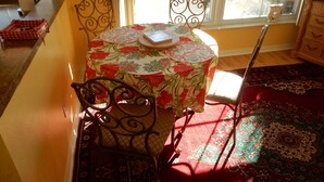 Un coin repas avec une table recouverte d’une nappe à motifs floraux, entourée de chaises en métal.