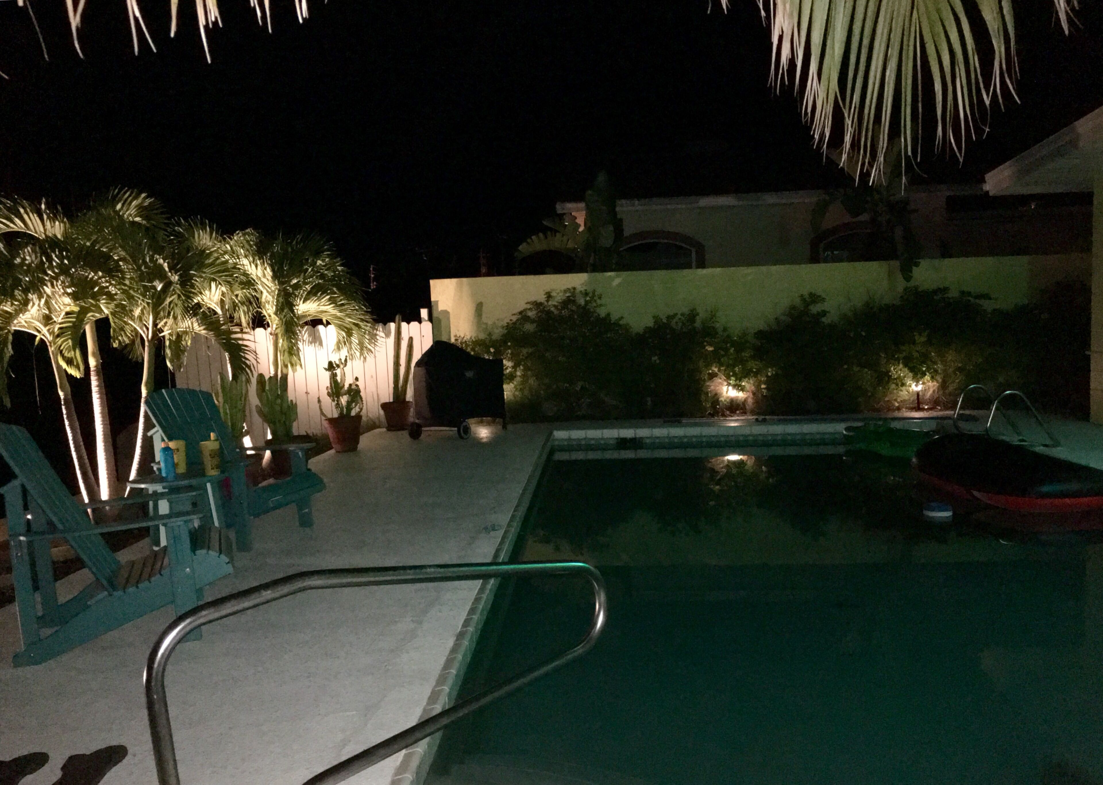 A nighttime pool area with lounge chairs, a small pool, and potted plants.