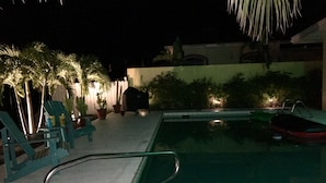 A nighttime pool area with lounge chairs, a small pool, and potted plants. - A GEM-Beach Cottage 4 BR,Heated Pool on Canal, 1 Block To Village, Walk to Beach (Sarasota)
