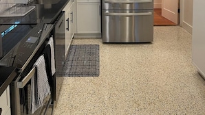 A modern kitchen with stainless steel appliances, white cabinets, and a black countertop. - A GEM-Beach Cottage 4 BR,Heated Pool on Canal, 1 Block To Village, Walk to Beach (Sarasota)