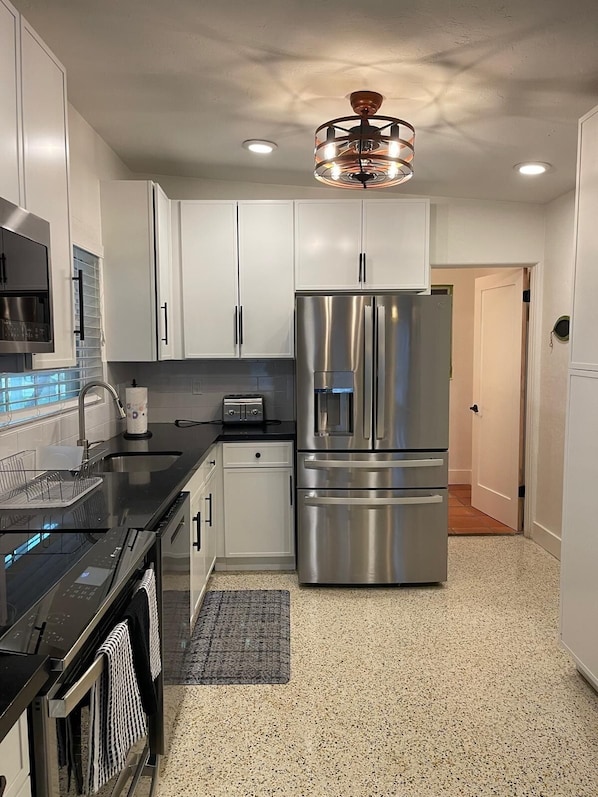 A modern kitchen with stainless steel appliances, white cabinets, and a black countertop.