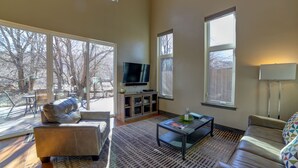 A spacious living room with a leather sofa, a coffee table, and a TV on a stand. There are large windows providing natural light and a view of the outdoors. - 3B/2B Modern Downtown Moab Townhouse - Short Walk from the Heart of Downtown (Moab)