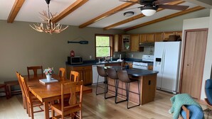 A spacious kitchen with wooden cabinets, a dining area with a large wooden table and chairs, and a ceiling fan. - Hidden Springs on Long Lake  -  Sleeping Bear Dunes National Lakeshore (Honor)