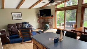 A living room with a fireplace, a television, and a dining area with a table and chairs. - Hidden Springs on Long Lake  -  Sleeping Bear Dunes National Lakeshore (Honor)