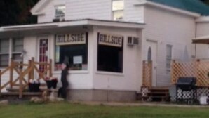 A white building with a green roof, two signs reading "HillSide," and a wooden fence in front. - Hillside Motel (Lake George)