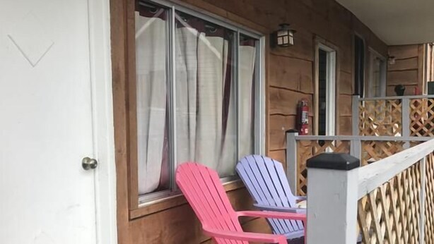A wooden deck with two Adirondack chairs, a white door, and a window with curtains. - Hillside Motel (Lake George)