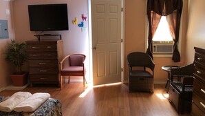 A bedroom with a bed, dresser, television, and a door leading to another room. - Hillside Motel (Lake George)