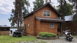 A wooden cabin with a sloped roof, a porch, and a small deck overlooking a body of water. - Beautiful Lakefront Property Minutes From The Kenai River And Soldotna (Soldotna)
