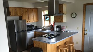 A kitchen with wooden cabinets, a stainless steel refrigerator, a microwave, a gas stove, a sink, and two wooden stools. - Beautiful Lakefront Property Minutes From The Kenai River And Soldotna (Soldotna)