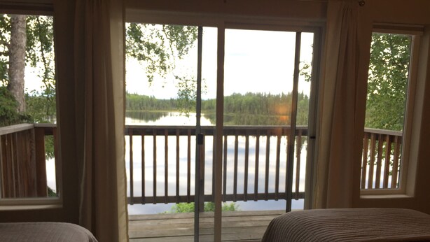 A room with a large window overlooking a lake, a wooden deck, and two beds. - Beautiful Lakefront Property Minutes From The Kenai River And Soldotna (Soldotna)