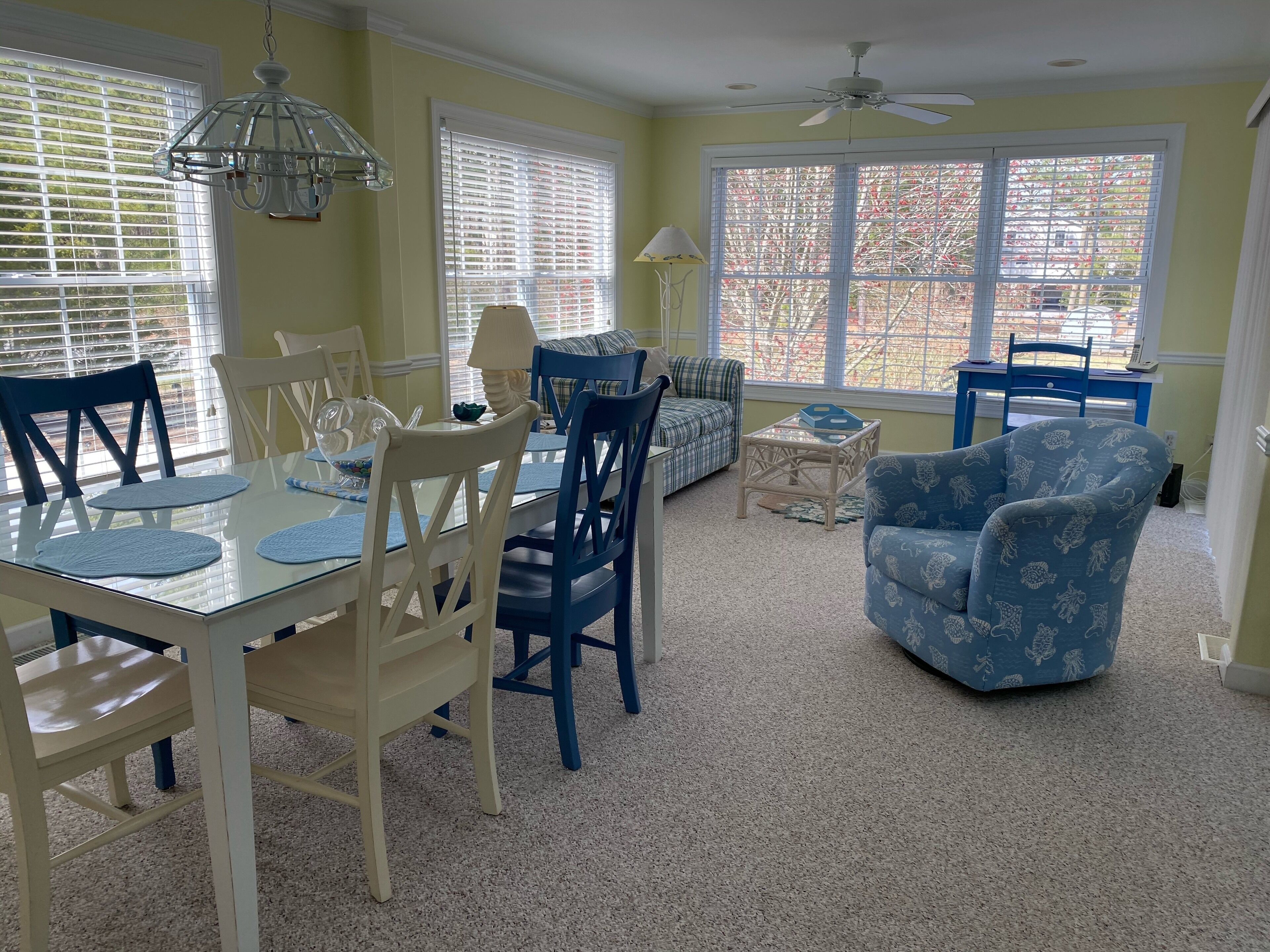 A dining area with a glass table, chairs, and a ceiling fan.
