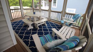 Una terrazza esterna coperta con pavimento a motivi blu, mobili bianchi e vista su una casa sullo sfondo.
