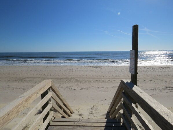 Un muelle de madera que conduce a una playa con cielo despejado y océano.