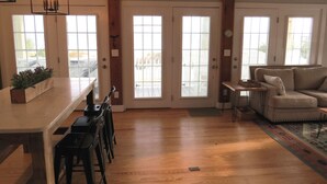 A spacious living area with a wooden floor, a kitchen counter, and a seating area with a sofa and chairs. - "The Palms" Oceanfront on Topsail Island, 2 BR - 2 BA Beach House - Awesome View (North Topsail Beach)