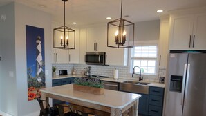 A modern kitchen with a central island, bar stools, a stainless steel refrigerator, and pendant lighting. - "The Palms" Oceanfront on Topsail Island, 2 BR - 2 BA Beach House - Awesome View (North Topsail Beach)