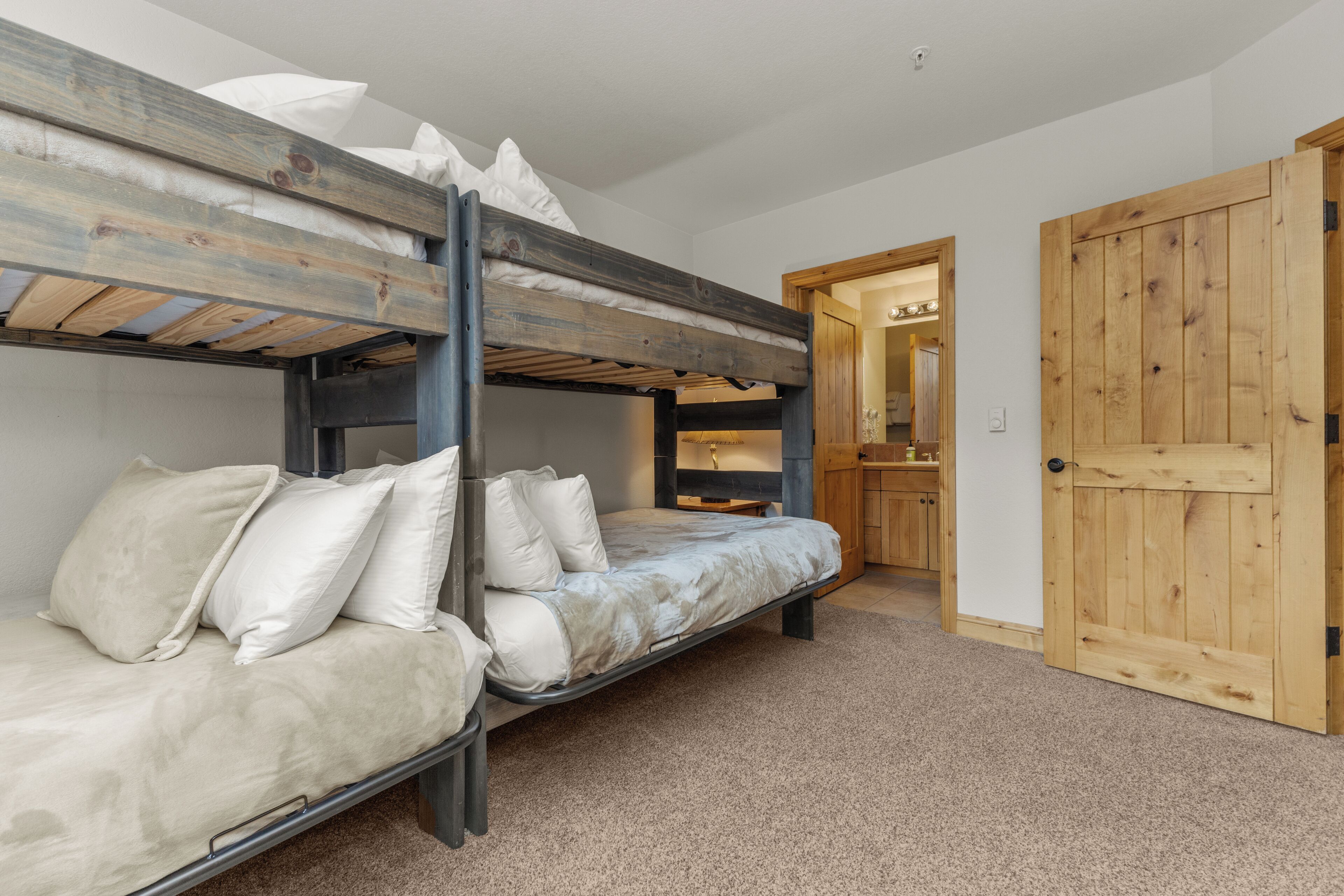 A bunk bed room with a wooden door and a carpeted floor.