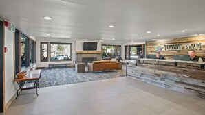 Un espace d’accueil moderne, doté d’un comptoir de réception en bois, d’une cheminée et de grandes fenêtres offrant une vue sur l’extérieur.