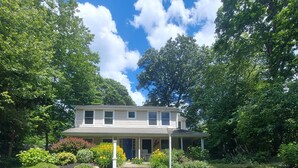 A two-story house with a front porch, surrounded by a well-maintained garden with various plants and flowers. - Cozy Escape in Pettaquamscutt Neighborhood - Your Ideal Narragansett Getaway (Narragansett)