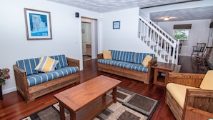 A spacious living room with two sofas, a coffee table, and a staircase leading to another level. - Cozy Escape in Pettaquamscutt Neighborhood - Your Ideal Narragansett Getaway (Narragansett)