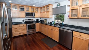 A modern kitchen with wooden cabinets, stainless steel appliances, and a black granite countertop. - Cozy Escape in Pettaquamscutt Neighborhood - Your Ideal Narragansett Getaway (Narragansett)