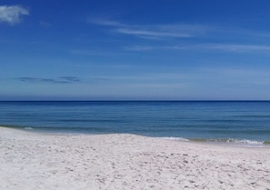 A beach with white sand and calm blue water under a clear sky.