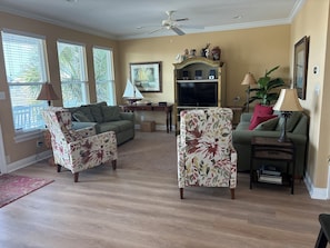 Ein Wohnzimmer mit einem grünen Sofa, floralen Ohrensesseln, einem Fernseher und einem Deckenventilator.