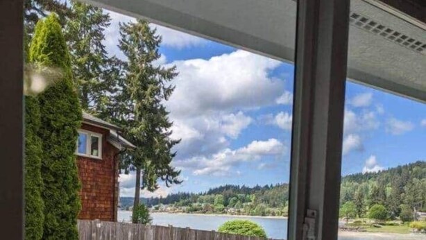A covered patio with outdoor furniture, a view of a lake, and a wooden fence. - Tide Cove Beachhouse in Poulsbo (Poulsbo)