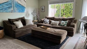 A living room with two brown sofas, a coffee table, and a large window with a view of greenery. - Tide Cove Beachhouse in Poulsbo (Poulsbo)