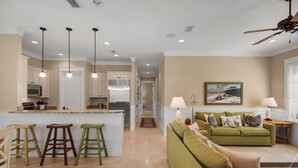 A spacious living area with a green sofa, a kitchen with white cabinetry, and a dining area with stools.