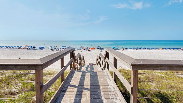 A wooden boardwalk leading to a beach with umbrellas and people.