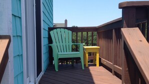 Una terraza de madera con una silla Adirondack verde y una pequeña mesa amarilla.